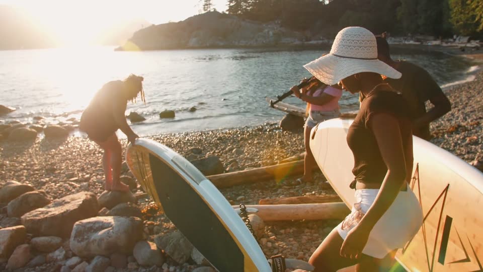 People carrying stand-up paddleboards toward the water